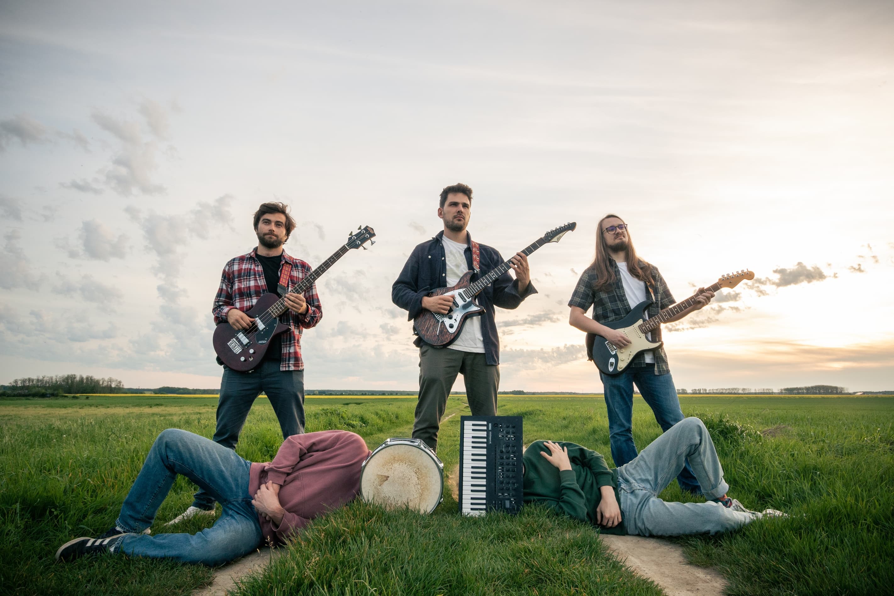 Group members in a field holding their instrument. Both the drumer and the pianist have their instrument in front of their head